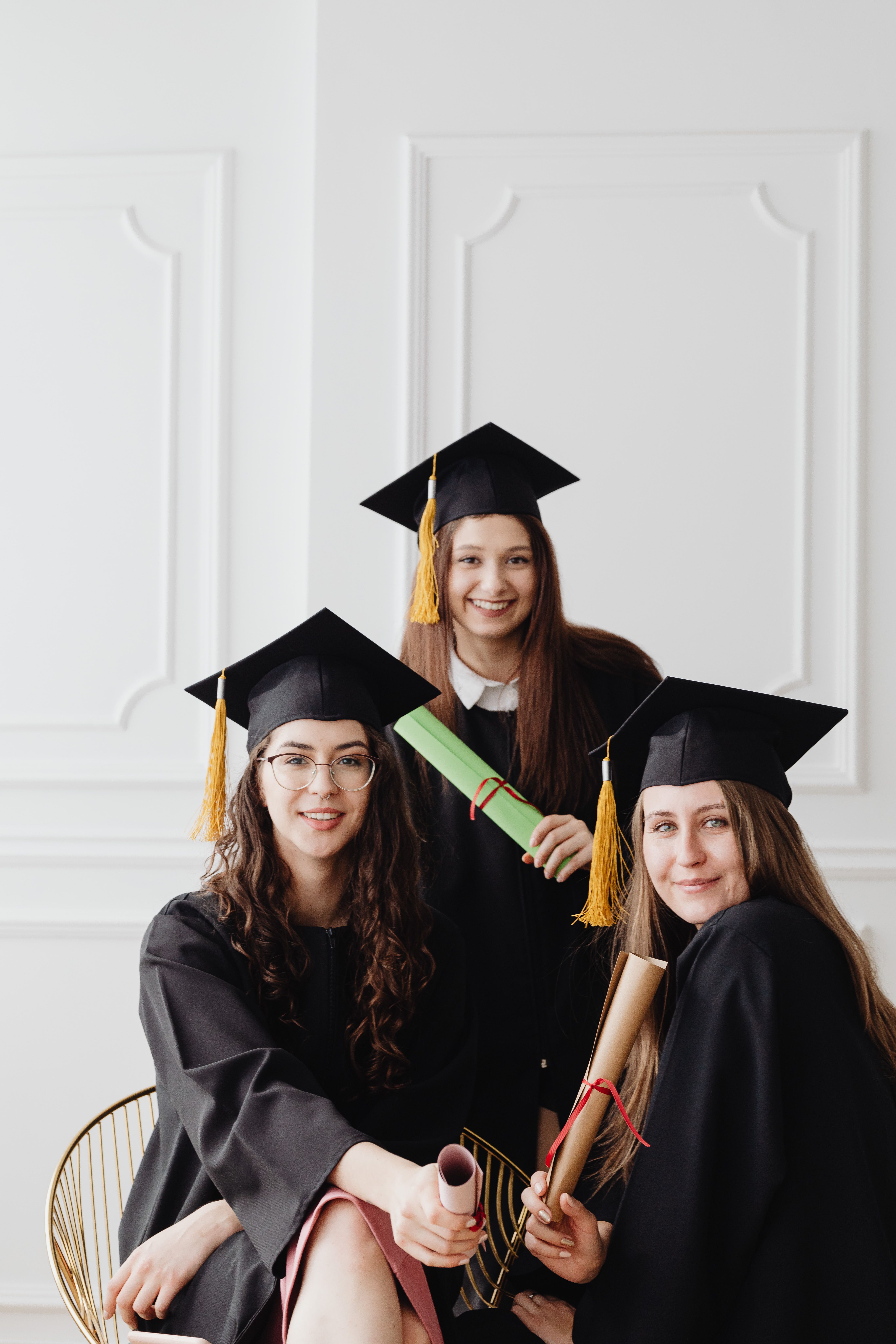 Graduate wearing a black mortarboard graduation cap with gold tassel, raising the cap during commencement